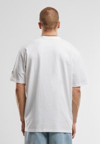White cotton t-shirt with a crew neck and short sleeves, featuring a relaxed fit and subtle black graphic detail on the left sleeve.