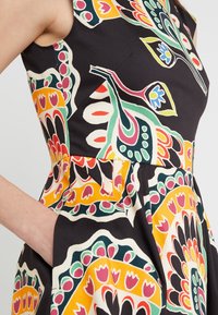 Mustapuku, jossa on kirkkaat kukkakuviot punaisena, vihreänä, sinisenä ja keltaisena. Sisältää istuvan yläosan ja taskut sivuilla.