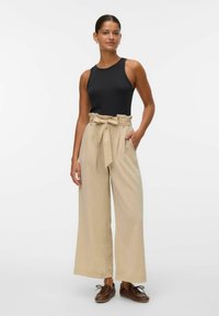 Svart ärmlös linne topp parat med högmidjade, vida beige byxor med knytbälte och sidfickor. Bruna snörskor.