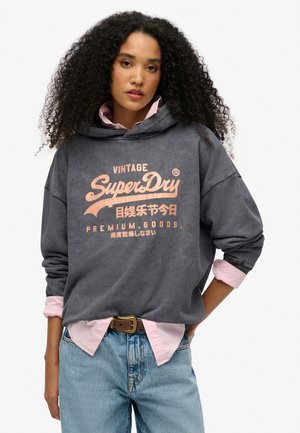 Hete grafietgrijze hoodie met een voorprint in perzik, voorzien van een kangoeroezak en een losse pasvorm. Gelaagd over een lichtroze shirt. Spijkerbroek.