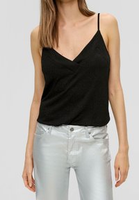 Haut noir sans manches avec un décolleté en V profond et une légère brillance ; porté avec un pantalon argenté brillant et ajusté.