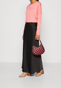 Schwarzer Satin-Maxi-Rock, hellrosa Langarmshirt, Handtasche mit rot-schwarzem Karomuster und beigen, strukturierten Stiefeletten mit Absatz.