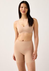 Beige saumattomat rintaliivit ja korkeat shortsit. Sileä kangas, v-mallinen design ja minimaaliset saumat. Mukava istuvuus ja kevyt rakenne.