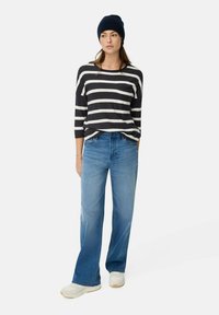 Schwarz-weiß gestreiftes Langarmhemd mit Brusttasche, kombiniert mit hellblauen weiten Jeans und weißen Sneakers. Beanie-Mütze inklusive.