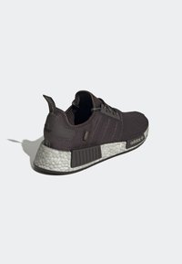 Svarta Adidas NMD-sneakers med strukturerad vit sula, svart hälflik och svarta sidopaneler mot en vit bakgrund, vinklad bakre vy.