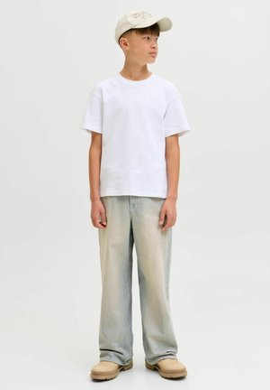 Witte katoenen t-shirt, losse pasvorm, gecombineerd met lichtblauwe jeans met een gradient. Beige schoenen en een lichtbruine pet maken de outfit compleet.
