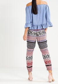 Top azzurro chiaro a spalle scoperte con orlo arricciato abbinato a pantaloni patterned con disegni geometrici rossi, neri e bianchi.