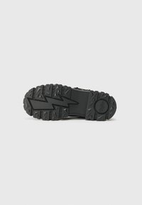 Black rubber shoe sole with a zigzag pattern, featuring deep treads for traction and textured surfaces for grip.