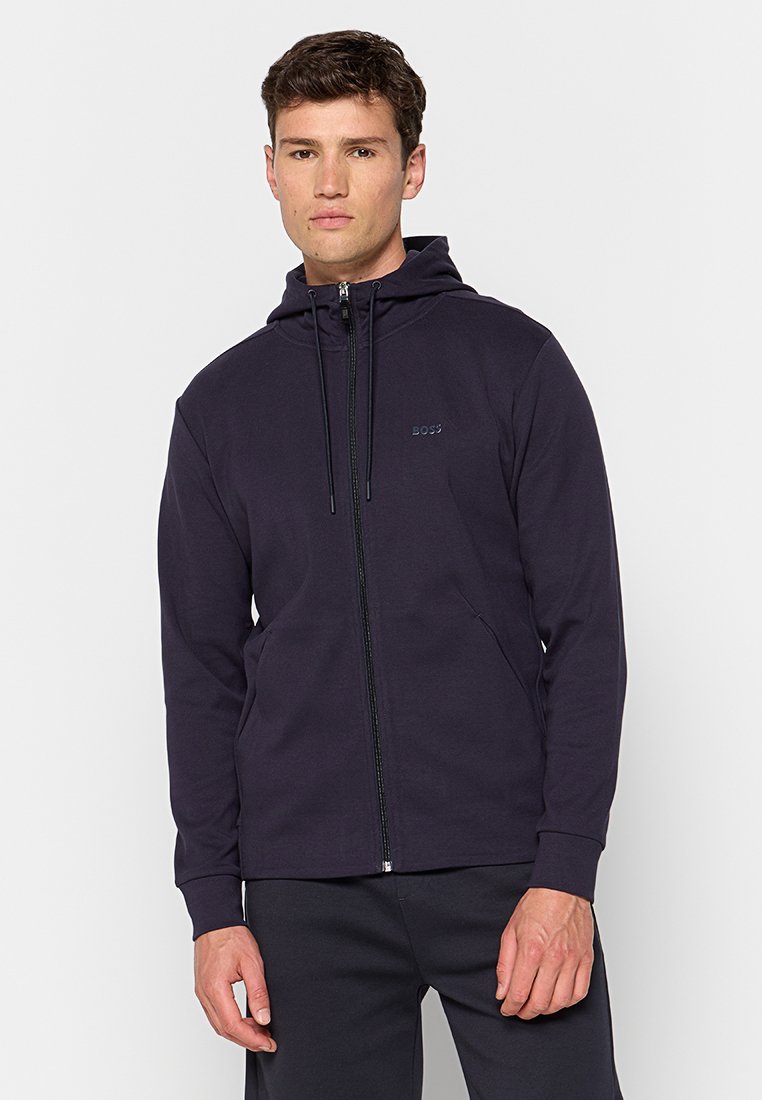 Felpa con zip di colore blu navy realizzata in un tessuto elastico con una texture morbida. Presenta un cappuccio regolabile con cordino e tasche laterali. Logo visibile sul petto.