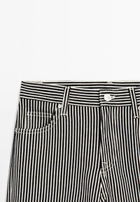 Pantaloni in denim a righe bianche e nere con design a gamba dritta, tasca frontale e cuciture a contrasto con chiusura a bottone.