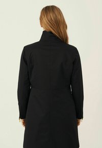 Black, long-sleeve coat with a high collar, fitted silhouette, and zipper details on the sleeves. Smooth fabric texture, minimalistic design.