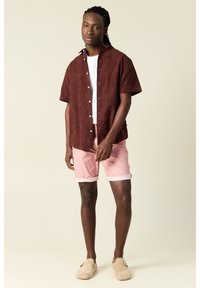 Lyhythihainen viininpunainen paita, jossa on teksturoitu kukkakuosi, yhdistetty vaaleanpunaisiin shortseihin ja beigeihin liukuvasti kenkäisiin. Yksinkertainen, rento malli.