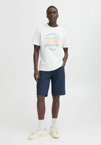 White graphic t-shirt with "DENIM AUTHENTIC IN STYLE" in orange and blue, paired with navy shorts and off-white sneakers.