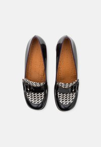 Chaussures en cuir verni noir avec un bout en tissu à motif pied-de-poule et une boucle décorative sur un côté. Texture lisse.