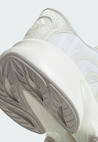 Baskets de sport blanches avec une tige en tissu texturé, une semelle en caoutchouc lisse, un motif de bande de roulement défini et des accents gris subtils sur le talon.