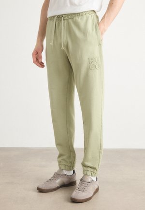 Pantalon de survêtement vert clair avec une taille élastique et cordon de serrage. Présente un logo "HUGO" brodé, des chevilles resserrées et une coupe décontractée.