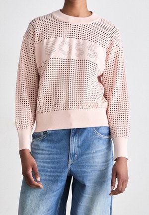 Pull en maille rose clair à motifs perforés avec le texte "BOSS" sur la poitrine, porté avec un jean bleu délavé taille haute.