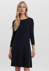 Robe en tricot bleu marine avec un col rond, des manches longues et une forme évasée, présentant une texture lisse et un design minimaliste.