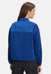 Niebieska kurtka z kordurojowej tkaniny z pionowym ryflem, lekko oversize'owy fason, kołnierz i mankiety na guziki. Tył ma prosty wzór panelowy.
