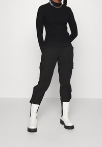 Svart ribbad långärmad topp i kombination med svarta cargobyxor som har sidofickor. Nakenet fulländas med vita ankelskor.