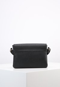 Borsa a tracolla in pelle sintetica nera con design semplice, patta pieghevole e tracolla regolabile. Dettaglio in metallo dorato sul lato.