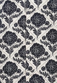 Tkanina w kwiatowy wzór z dużymi czarnymi różami na kremowym tle, z guzikiem na środku. Faktura przypomina tkaną.