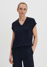 Top in misto lana blu navy con scollo a V, maniche corte e vestibilità rilassata, caratterizzato da una superficie testurizzata e un orlo leggermente curvo.