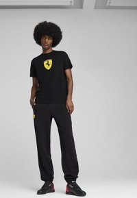 Čierne tričko s žltým logom Ferrari, v kombinácii s čiernymi teplákmi s žltým logom a čierno-červenými topánkami. Jednoduchý dizajn.