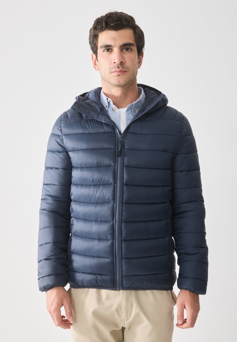Námořnická puffer bunda s horizontálním prošitím a kapucí, vyrobená z lehkého materiálu. Přední zip a dvě boční kapsy.