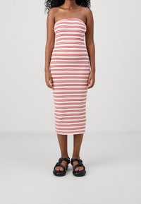 Bezramkowa sukienka midi w białym kolorze z czerwonymi pionowymi paskami, dopasowany krój, gładki materiał. Czarne sandały z grubymi paseczkami i zaokrąglonym fasonem.