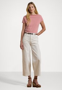 Top rosa a maniche corte abbinato a pantaloni ampi a vita alta color crema. Sandali a zeppa marroni e una cintura argentata accentuano l'outfit.