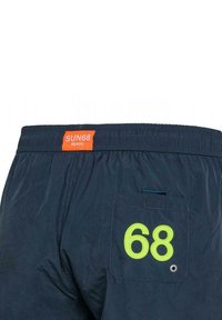Costumi da bagno blu navy con un'etichetta arancione che legge "SUN68 BEACH" in vita. Presentano una tasca sul retro con un dettaglio ricamato "68" di colore verde brillante.