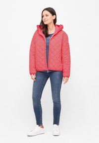 Chaqueta acolchada con capucha en un brillante color coral. Cuenta con un cierre frontal, bolsillos laterales y un patrón de diamante cosido. Combina con una blusa azul y jeans.
