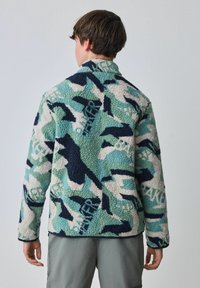 Vilnas jaka ar daudzkrāsainu maskēšanās rakstu tērkaza, tumši zila un krēmkrāsas toņos, ar augstu apkakli un garām piedurknēm.