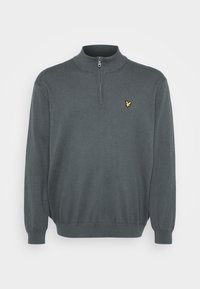 Sweatshirt à col zip grise en maille douce. Il présente un col et des poignets côtelés avec un petit logo jaune sur la poitrine.