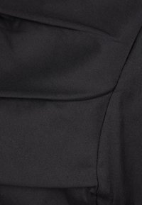 Gros plan d'un tissu noir avec des coutures visibles et des lignes de couture, mettant en valeur la texture et les détails de la confection sur mesure.