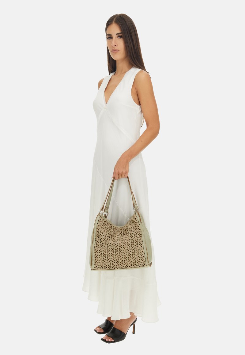 Abito bianco senza maniche con scollatura a V e orlo stratificato. La modella porta una borsa in pelle beige perforata con dettagli verdi e sandali neri con le punte scoperte.
