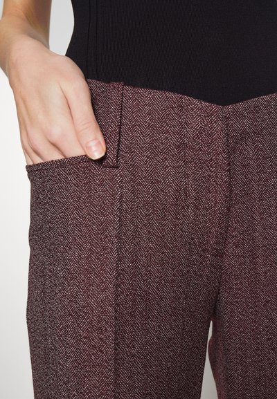 Καφέ παντελόνι σε σχέδιο καπιτονέ με υφή, διαθέτει μπροστινή τσέπη και κομψή γραμμή. Λεπτομέρεια στην περιοχή της τσέπης.
