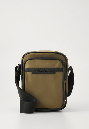 Sac en bandoulière rectangulaire vert olive en nylon, avec une sangle noire, des fermetures éclair et une étiquette en tissu de marque à l'avant.