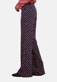 Långa byxor i marinblått tyg med ett mönster av rosa hjärtan. Har hög midja och utsvängd nederdel. Materialet har en slät textur.
