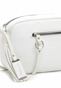 Hvid læder crossbody-taske med sølvlynlås, cirkulært metalvedhæng på frontlommen og hvid kvastdetalje på stroppen.