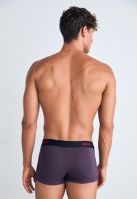 Boxer da uomo Hugo in viola scuro. Vita elastica con logo rosso, design aderente, texture liscia, lunghezza a metà coscia.