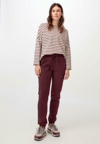 Gestreiftes Langarmtop in Creme und Burgundy, kombiniert mit burgundy Jogginghosen. Die Jogginghosen haben einen elastischen Bund und Bündchen an den Knöcheln.