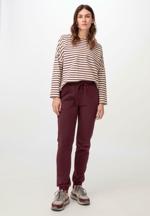Camiseta de manga larga a rayas en crema y burdeos, combinada con pantalones jogger burdeos. Los joggers tienen una cinturilla elástica y puños en los tobillos.