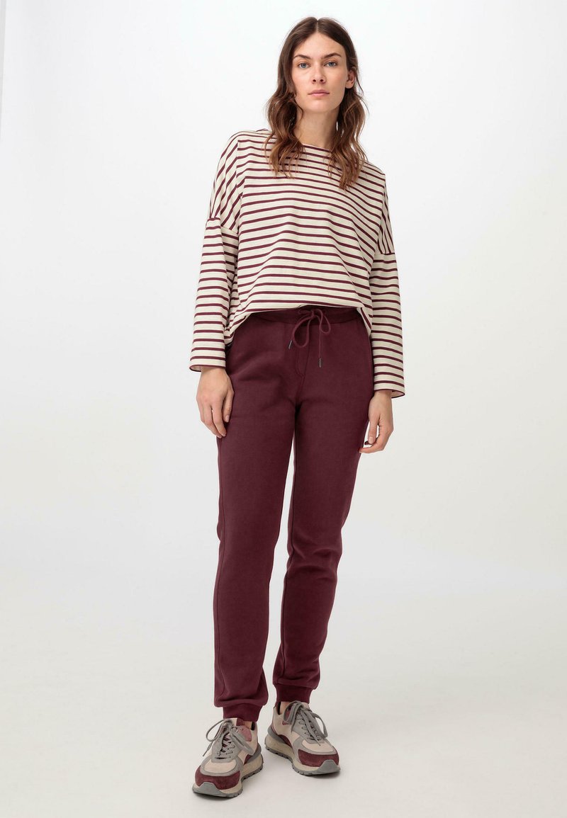 Gestreiftes Langarmtop in Creme und Burgundy, kombiniert mit burgundy Jogginghosen. Die Jogginghosen haben einen elastischen Bund und Bündchen an den Knöcheln.