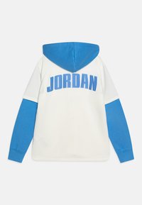 Sudadera con capucha que presenta un cuerpo blanco con mangas azules y capucha azul. "JORDAN" impreso en grandes letras azules en la parte posterior.