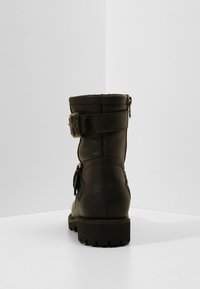 Svart läderankelstövel med texturerad yta, som har ett spänne, rund tå och en grov sula. Bakåtsikt mot en enkel bakgrund.