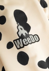 Beżowy materiał w czarne kropki; z graficznym logo "WeeDo" w kolorze czarnym i szarym. Gładka tekstura, swobodny design.
