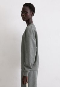 Szary sweatshirt o luźnym kroju, z prążkowanymi mankietami i okrągłym dekoltem, noszony z pasującymi spodniami. Gładka tekstura i prosty design.