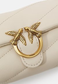 Clutch in pelle beige con texture trapuntata, dotata di chiusura circolare in tono oro a forma di due uccelli, con ali incise.